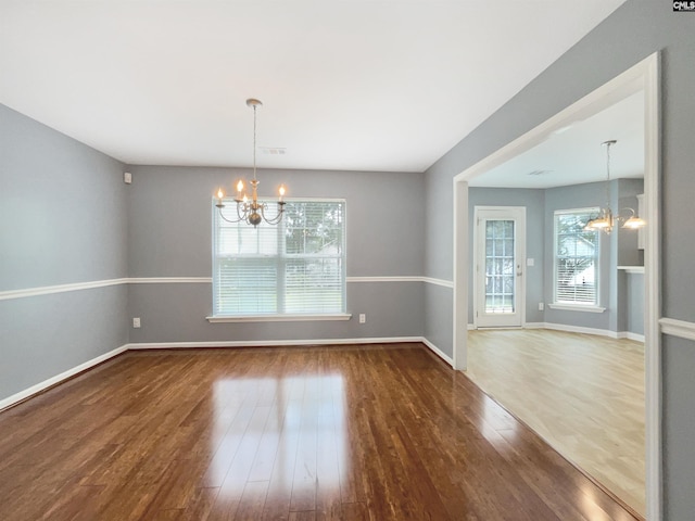 unfurnished dining area with a healthy amount of sunlight, an inviting chandelier, and dark wood-type flooring