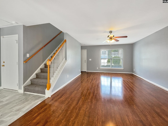 unfurnished living room with ceiling fan, baseboards, wood finished floors, and stairs