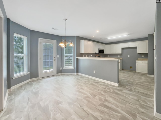 kitchen with white cabinetry, stainless steel microwave, a peninsula, and a chandelier