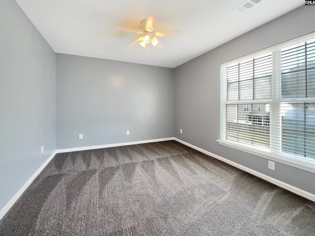 empty room with baseboards, visible vents, dark carpet, and ceiling fan