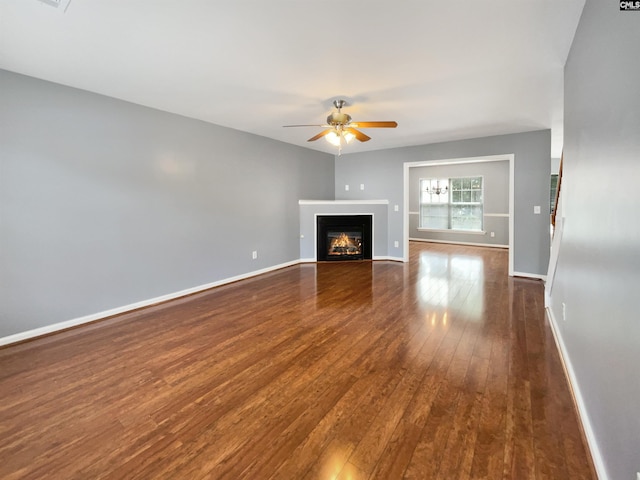 unfurnished living room featuring a glass covered fireplace, a ceiling fan, dark wood-type flooring, and baseboards