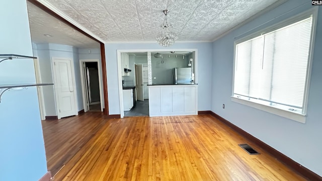 unfurnished living room with crown molding, a notable chandelier, and hardwood / wood-style flooring