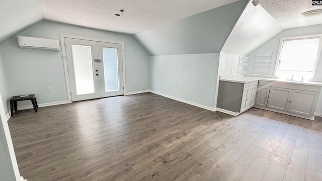 additional living space featuring vaulted ceiling, a textured ceiling, hardwood / wood-style flooring, and a wall unit AC