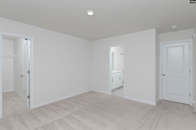 unfurnished bedroom featuring ensuite bath, light carpet, a walk in closet, and a closet