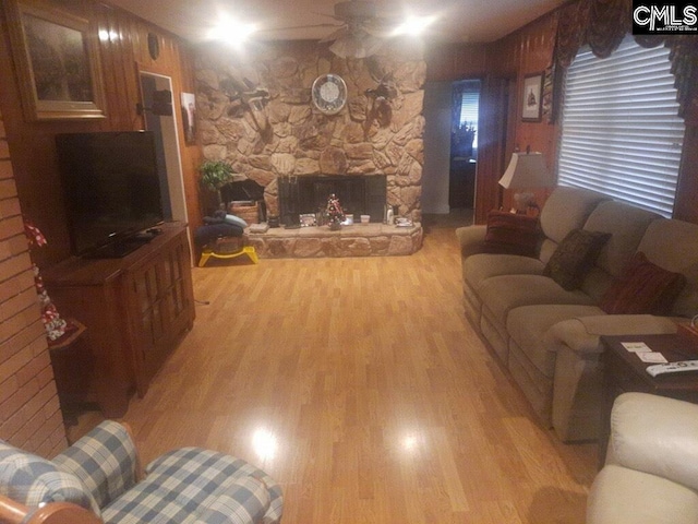 living room featuring light hardwood / wood-style flooring, wood walls, and a stone fireplace