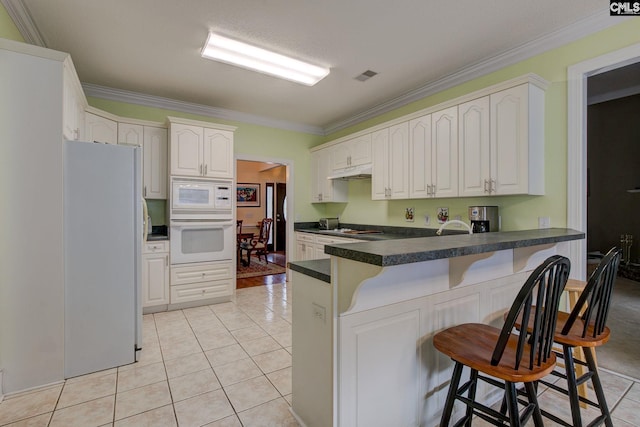 kitchen featuring white appliances, a kitchen breakfast bar, light tile patterned flooring, kitchen peninsula, and white cabinets