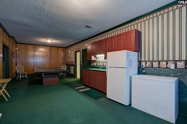 interior space featuring white refrigerator, sink, dark carpet, wood walls, and a textured ceiling