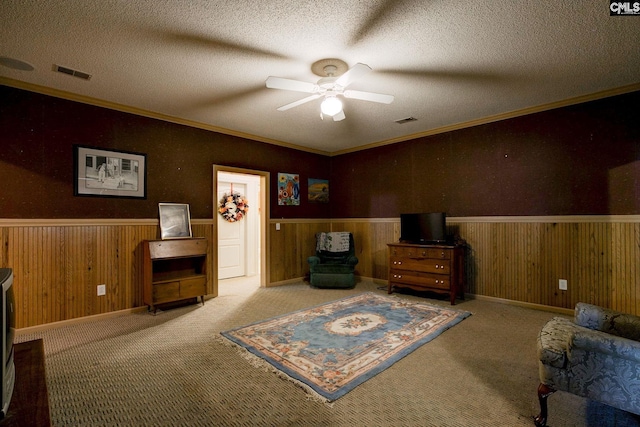 living area with ceiling fan, wooden walls, a textured ceiling, and ornamental molding