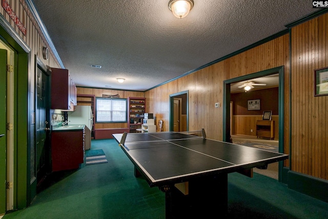 recreation room featuring a textured ceiling, dark colored carpet, and wooden walls