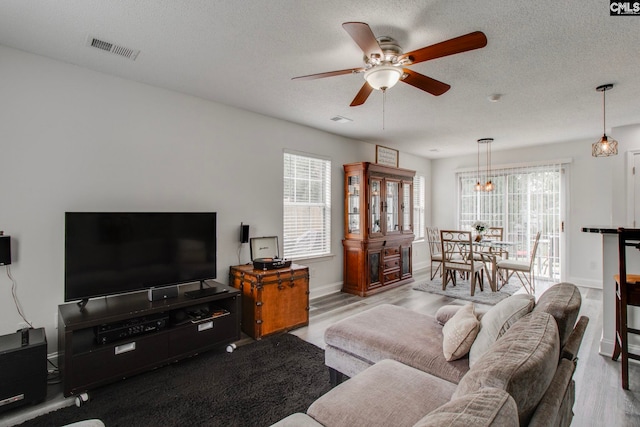 living area with visible vents, a ceiling fan, a textured ceiling, wood finished floors, and baseboards