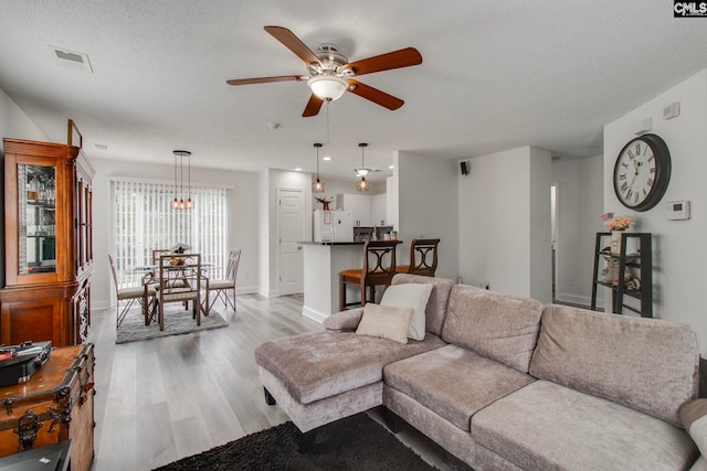 living area with baseboards, visible vents, light wood finished floors, ceiling fan, and a textured ceiling