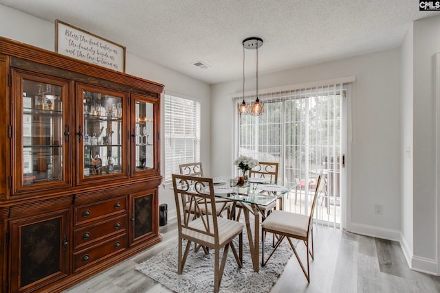 dining space with a textured ceiling, baseboards, visible vents, and light wood-type flooring