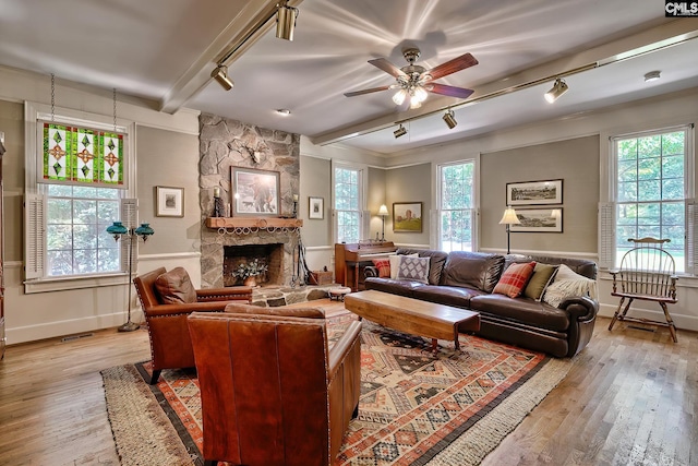 living room with rail lighting, ceiling fan, a stone fireplace, and light wood-type flooring