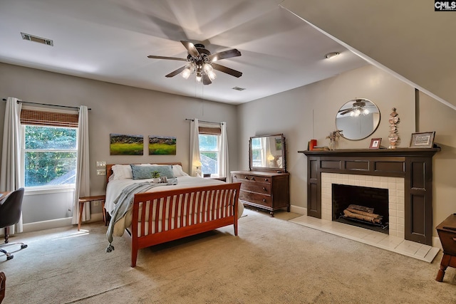 bedroom with light colored carpet, ceiling fan, and a tile fireplace