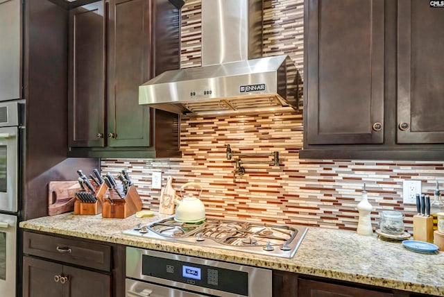 kitchen featuring backsplash, stainless steel appliances, light stone countertops, extractor fan, and dark brown cabinetry