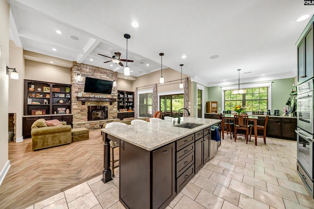 kitchen with a fireplace, light stone countertops, sink, an island with sink, and ceiling fan