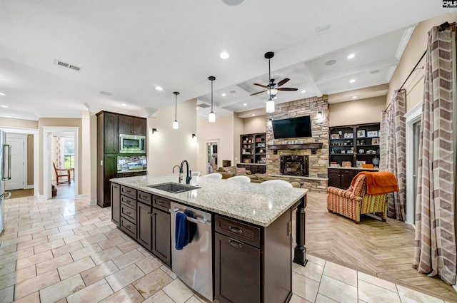 kitchen with a stone fireplace, appliances with stainless steel finishes, a kitchen island with sink, sink, and dark brown cabinetry