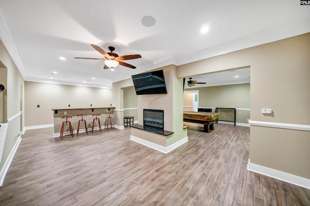 living room with ceiling fan, ornamental molding, light wood-type flooring, and a multi sided fireplace