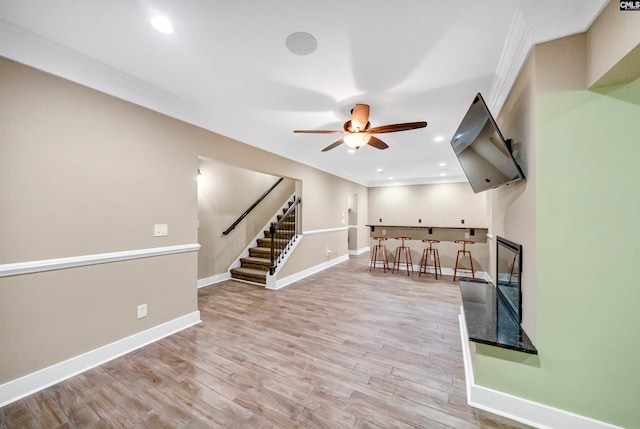 interior space with light wood-type flooring, ceiling fan, indoor bar, and ornamental molding