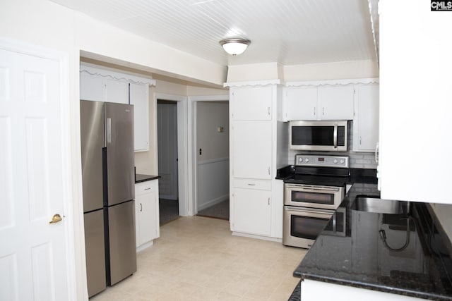 kitchen with stainless steel appliances, dark stone counters, and white cabinetry