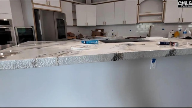 kitchen with kitchen peninsula, white cabinetry, stainless steel appliances, and tasteful backsplash