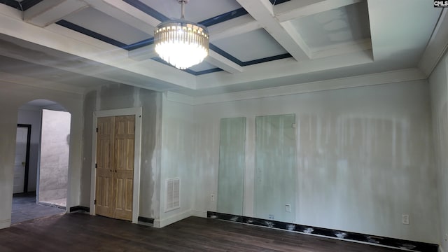 empty room featuring coffered ceiling, beamed ceiling, dark wood-type flooring, and an inviting chandelier