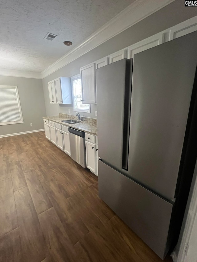 kitchen with dark hardwood / wood-style floors, appliances with stainless steel finishes, ornamental molding, light stone counters, and white cabinets