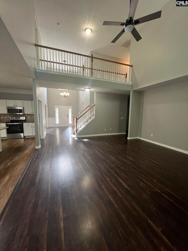 unfurnished living room with a textured ceiling, a high ceiling, dark hardwood / wood-style floors, and ceiling fan with notable chandelier