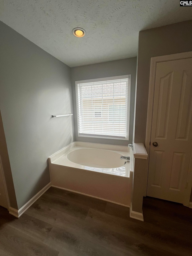 bathroom with a textured ceiling, wood-type flooring, and a tub