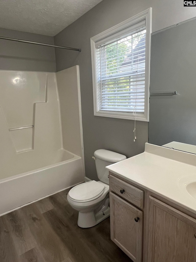 full bathroom with hardwood / wood-style floors, toilet, vanity, washtub / shower combination, and a textured ceiling