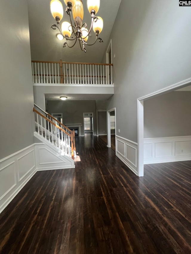 interior space with dark wood-type flooring, a towering ceiling, and a chandelier