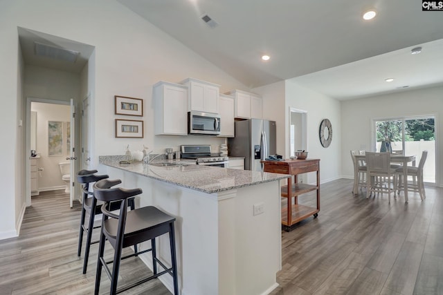 kitchen with kitchen peninsula, light wood-type flooring, stainless steel appliances, vaulted ceiling, and white cabinets