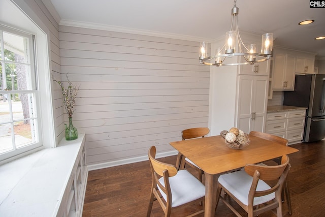 dining space featuring crown molding, dark wood-type flooring, an inviting chandelier, and wooden walls