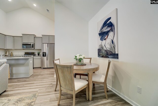 dining space with high vaulted ceiling and light hardwood / wood-style flooring