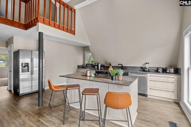 kitchen with appliances with stainless steel finishes, light wood-type flooring, white cabinetry, and a breakfast bar