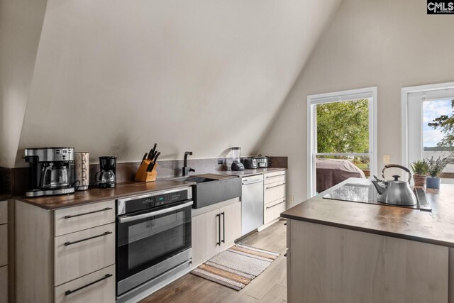 kitchen with appliances with stainless steel finishes, high vaulted ceiling, white cabinets, light wood-type flooring, and sink