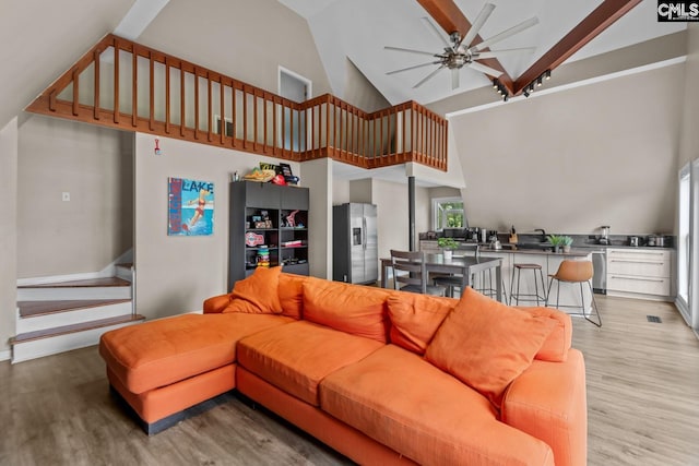 living room featuring light hardwood / wood-style flooring, ceiling fan, beamed ceiling, and high vaulted ceiling