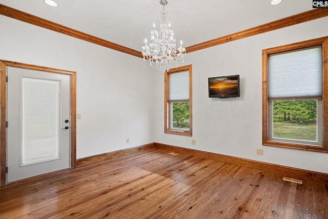 unfurnished room with light wood-type flooring, a healthy amount of sunlight, ornamental molding, and a chandelier