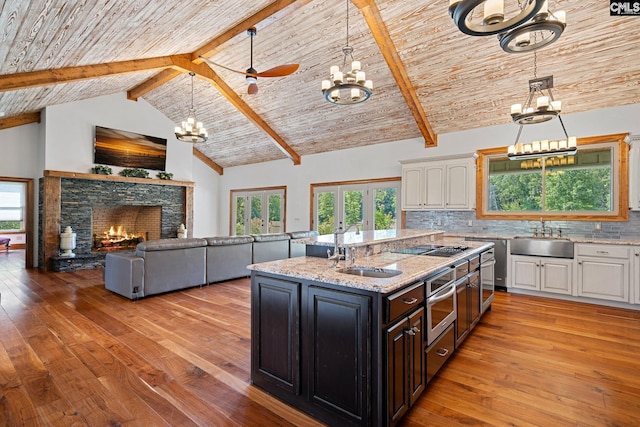 kitchen with a stone fireplace, white cabinets, ceiling fan with notable chandelier, and sink