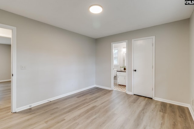 unfurnished bedroom featuring ensuite bath and light hardwood / wood-style floors