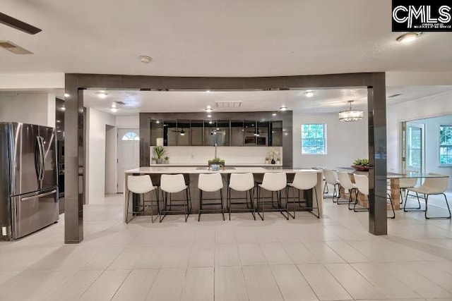 kitchen featuring hanging light fixtures, light tile patterned floors, a kitchen island, stainless steel refrigerator, and a breakfast bar area