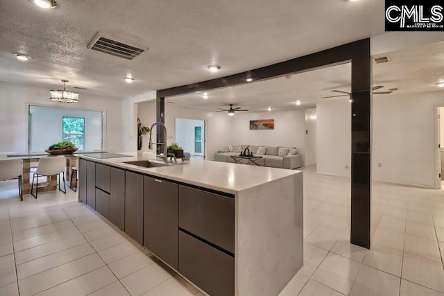 kitchen with ceiling fan with notable chandelier, light tile patterned floors, a textured ceiling, sink, and a spacious island