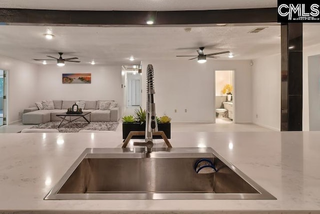 kitchen with light stone countertops, beam ceiling, sink, and ceiling fan