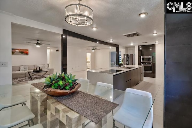 interior space with a large island with sink, ceiling fan with notable chandelier, stainless steel appliances, a textured ceiling, and sink