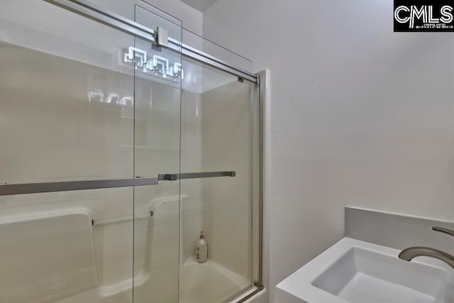 bathroom featuring a shower with door and sink