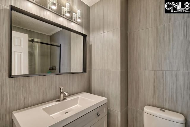 bathroom with vanity, tile walls, toilet, and a shower with door