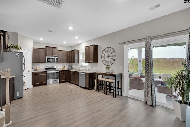 kitchen featuring dark brown cabinetry, sink, light hardwood / wood-style flooring, backsplash, and stainless steel appliances