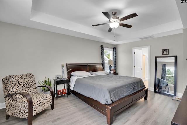 bedroom with ceiling fan, light wood-type flooring, and a raised ceiling