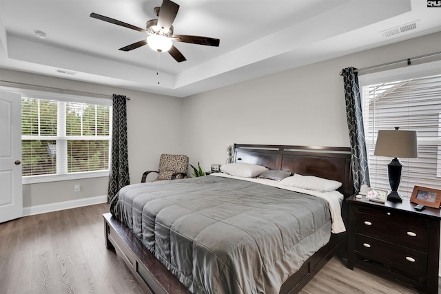 bedroom with light wood-type flooring, ceiling fan, and a raised ceiling