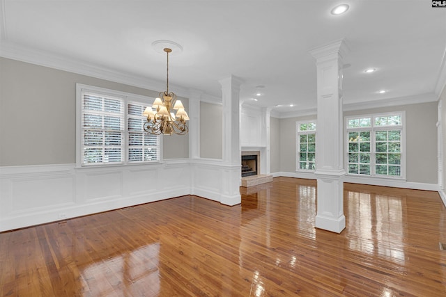 unfurnished living room featuring wood-type flooring, an inviting chandelier, decorative columns, and a healthy amount of sunlight